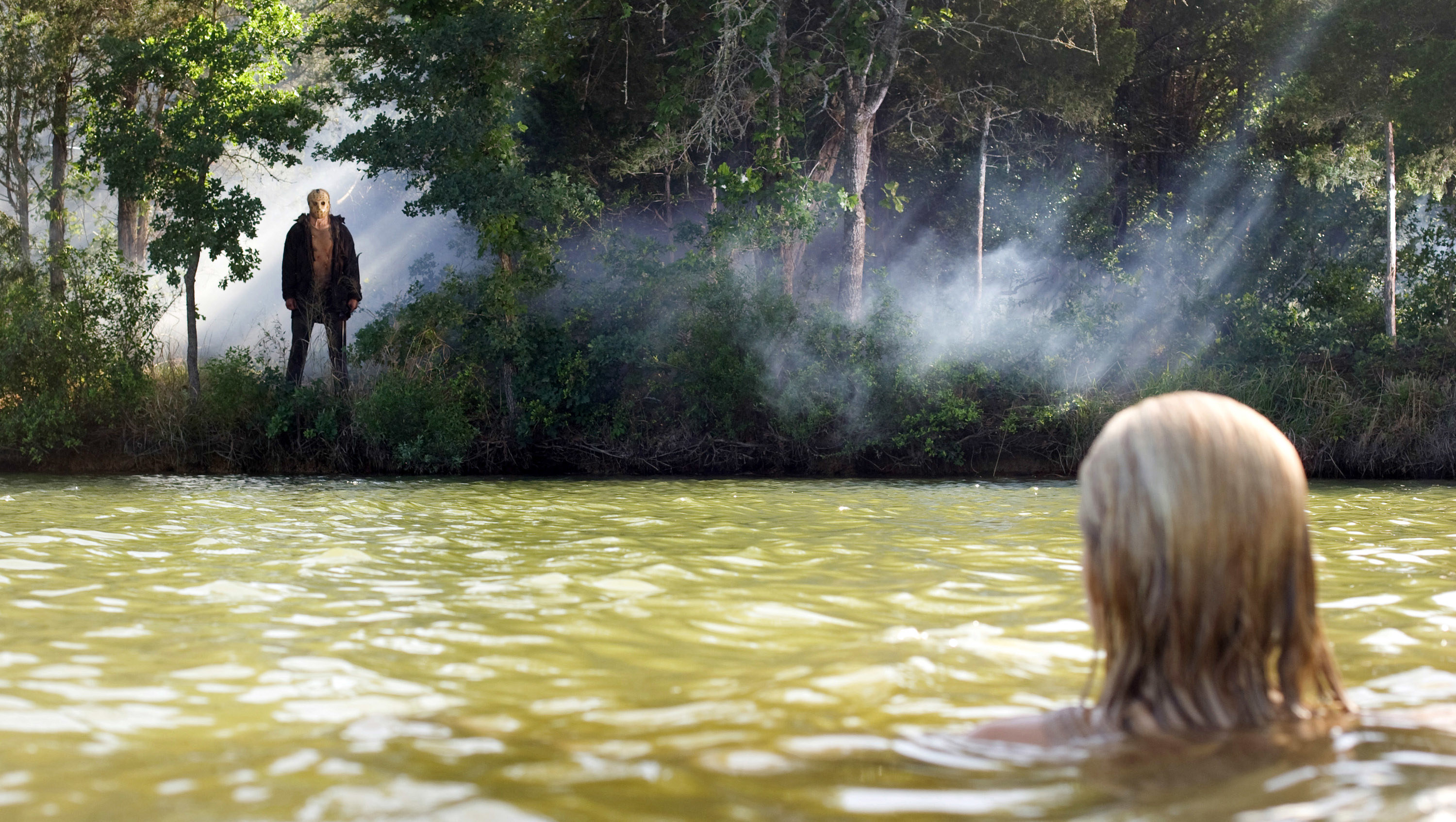 A woman swimming in a lake with Jason watching her from in the woods