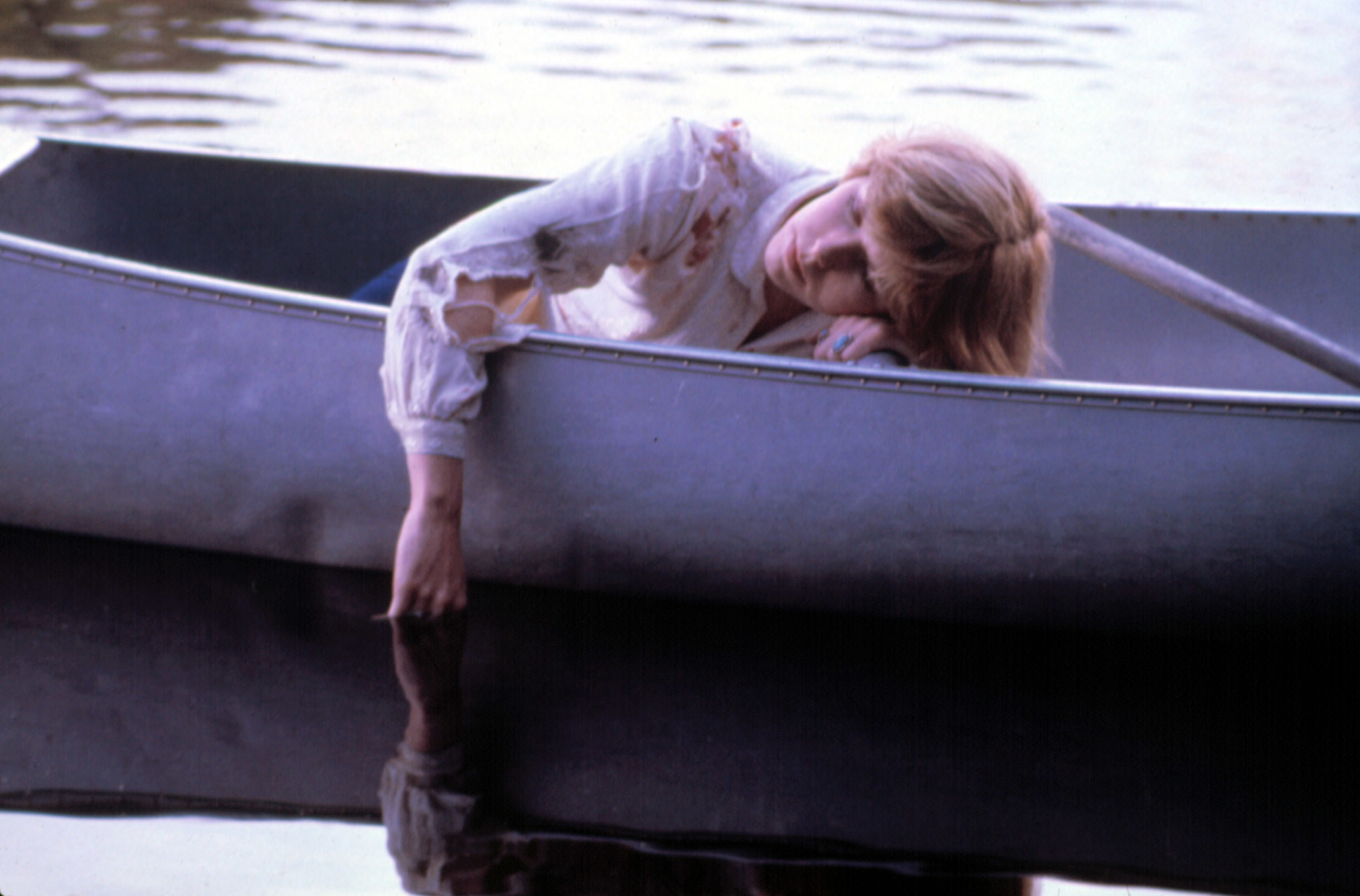 A woman sleeps in a boat with her hand dipped into the lake