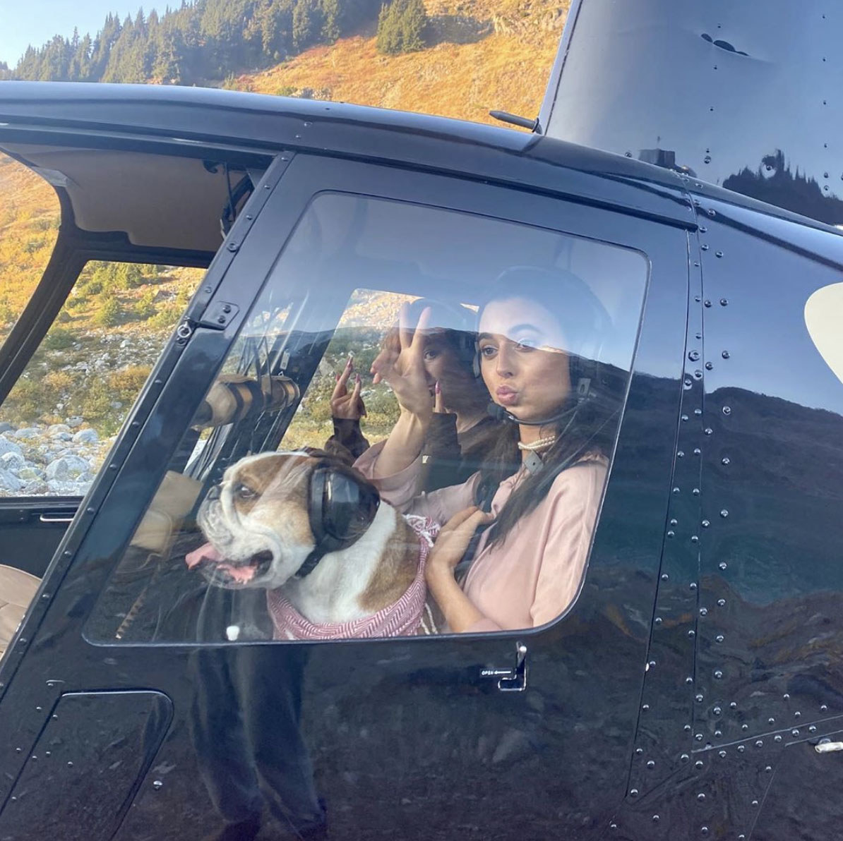 Reina holds up a peace sign while sitting in a helicopter with a dog in her lap