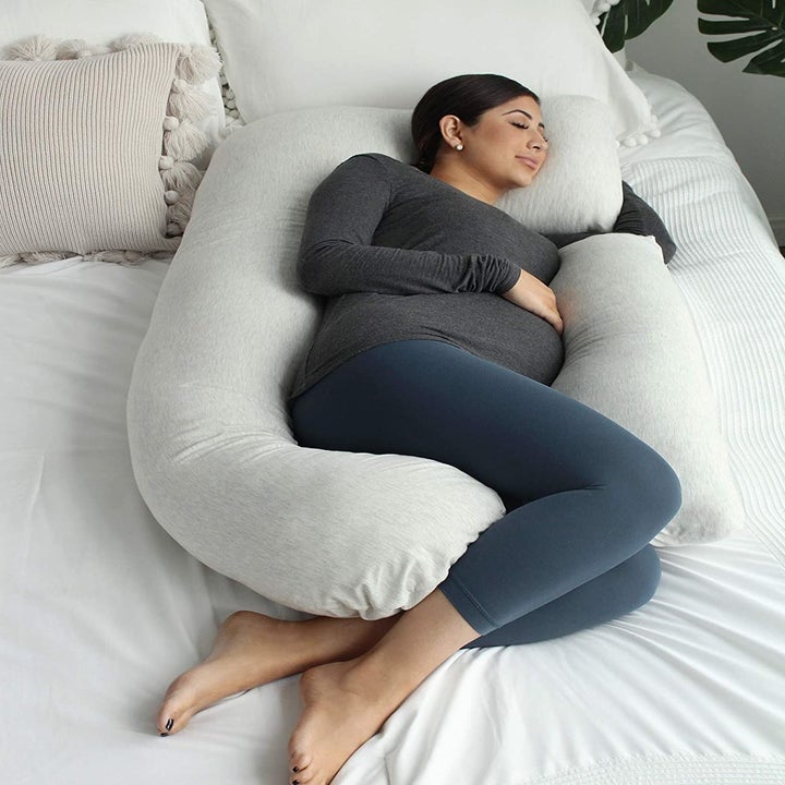 Pregnant model sleeping with the body pillow surrounding them, except for the space where it doesn't connect where they put their arm 
