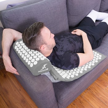 A model resting on a gray mat with circular acupressure spikes  on a couch