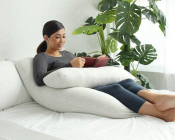 Pregnant model reading while propped on the pillow with part of the pillow under her book 