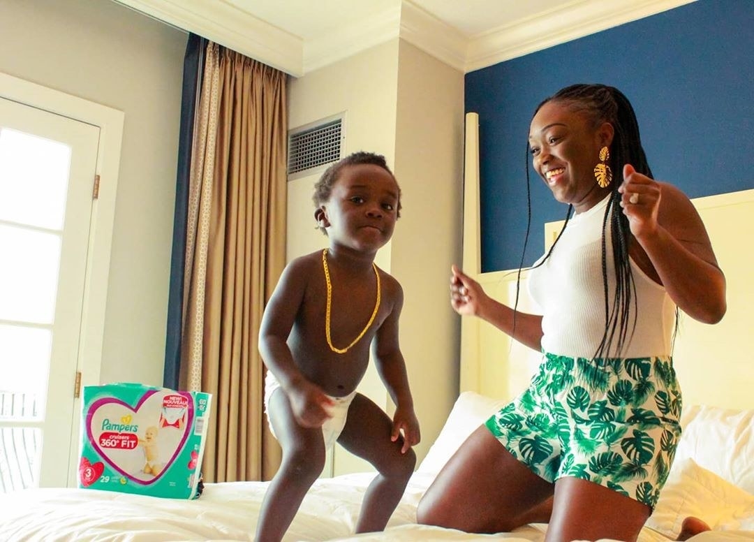 Mother and toddler son in diaper dancing together on bed