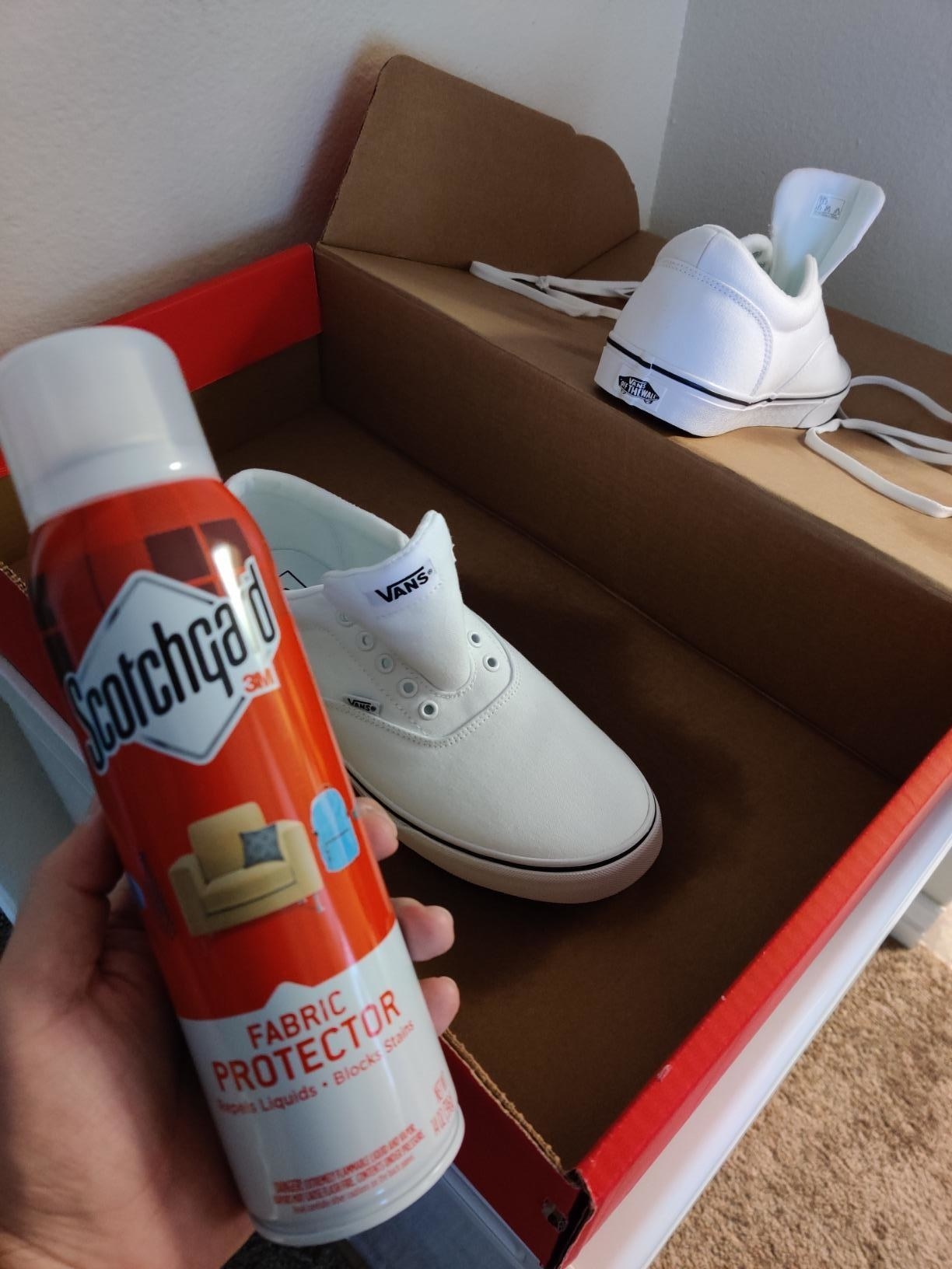 Reviewer holding up protective spray in front of a box of white shoes