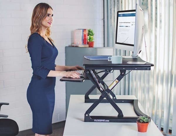 A person standing up and looking at their computer at eye-level with the standing desk on top of their desk