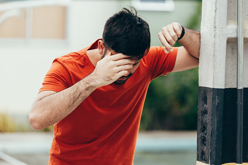 Man suffering from dizziness with difficulty standing up while leaning on wall.