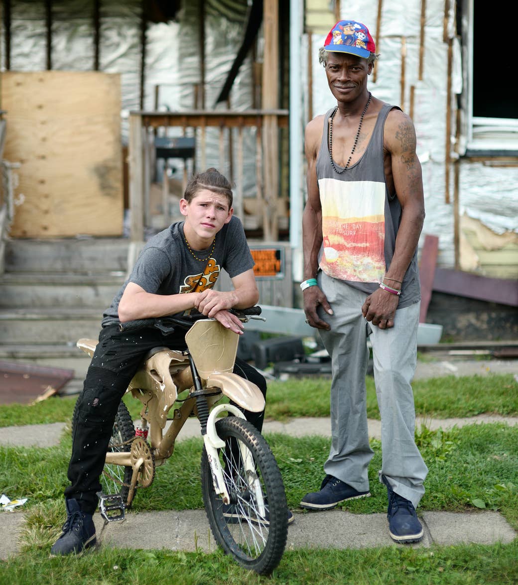 A boy on a bike and a man standing in front of a boarded-up house