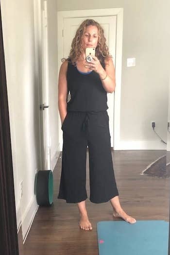 A mirror selfie of a reviewer wearing a black wide-leg jumpsuit standing next to a workout mat