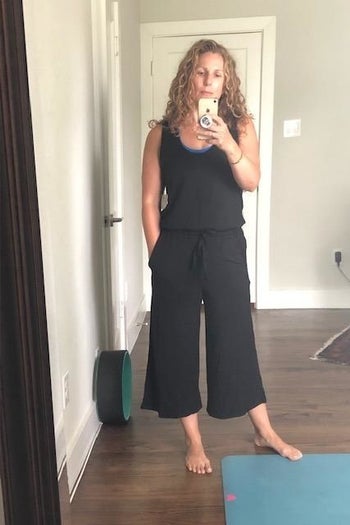 A mirror selfie of a reviewer wearing a black wide-leg jumpsuit standing next to a workout mat