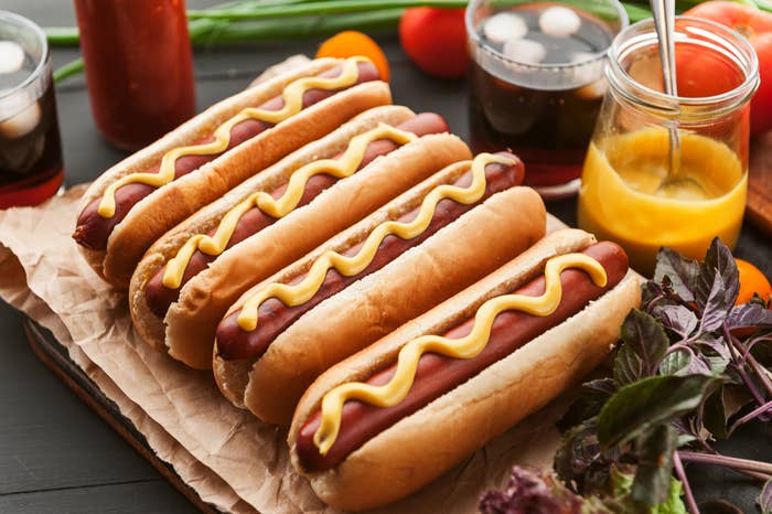 Four hot dogs in a line, each with an enticing line of mustard atop them