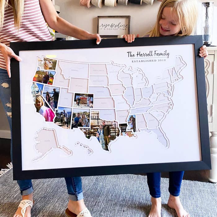 Two people holding a large frame of the U.S. map with some photos shaped to fit the states