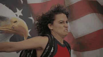 Ilana Glazer saluting an American flag emblazoned with a bald eagle in the Comedy Central series Broad City