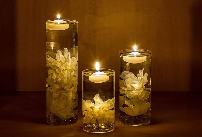 Three vases with flowers inside and candles floating on the water.