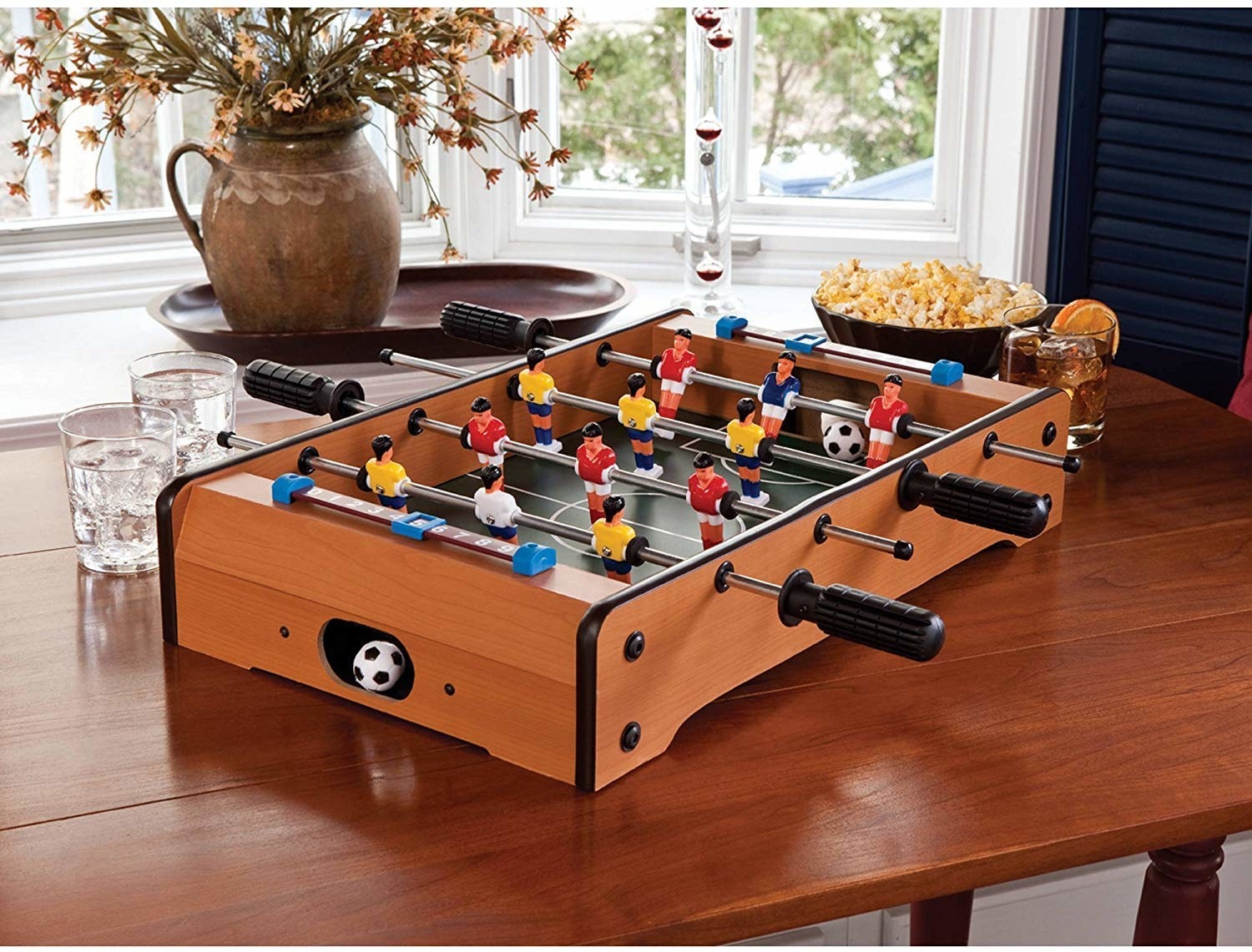 Foosball table kept on a dining table beside popcorn and drinks.