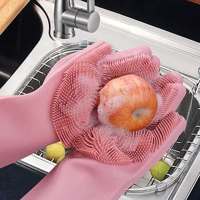 A person washing an apple with the silicone gloves.