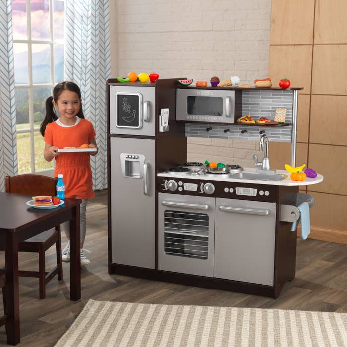 kid smiling while standing next to a play kitchen set