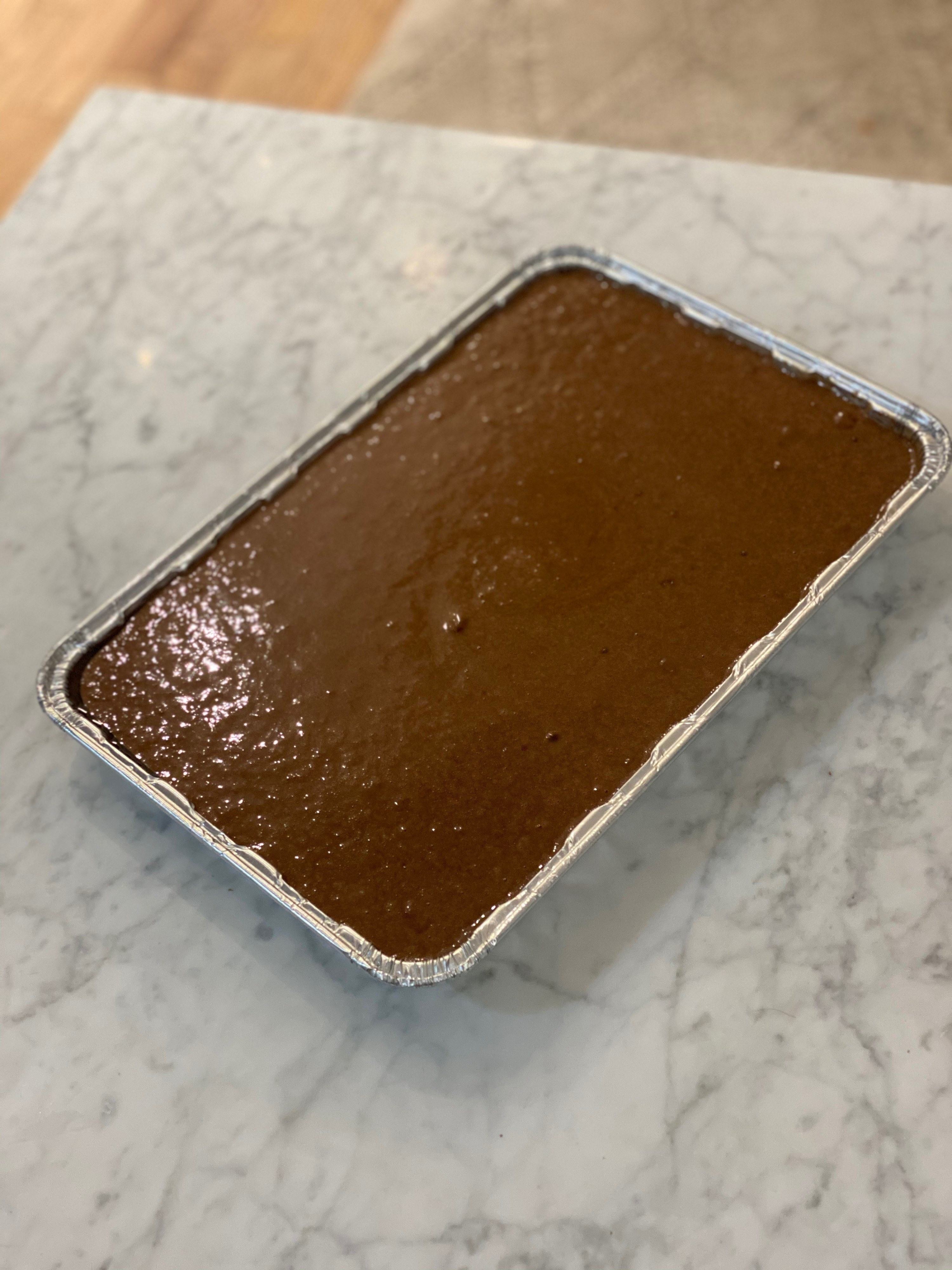Chocolate cake batter in an aluminum cake tray, ready for the oven.