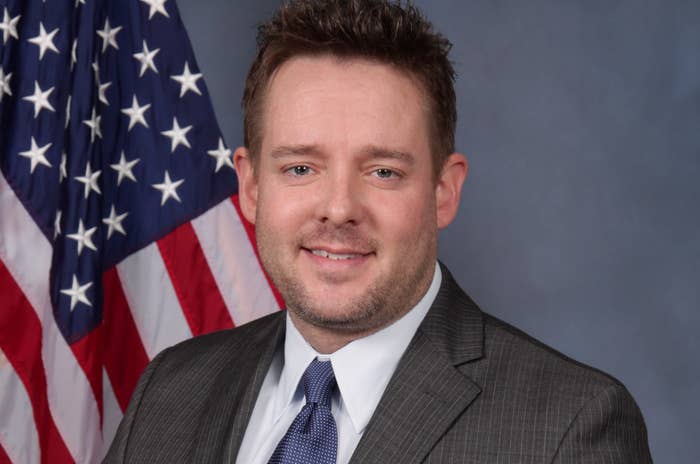 Jonathan Mattingly wears a suit and tie and smiles before the US flag in his official police picture