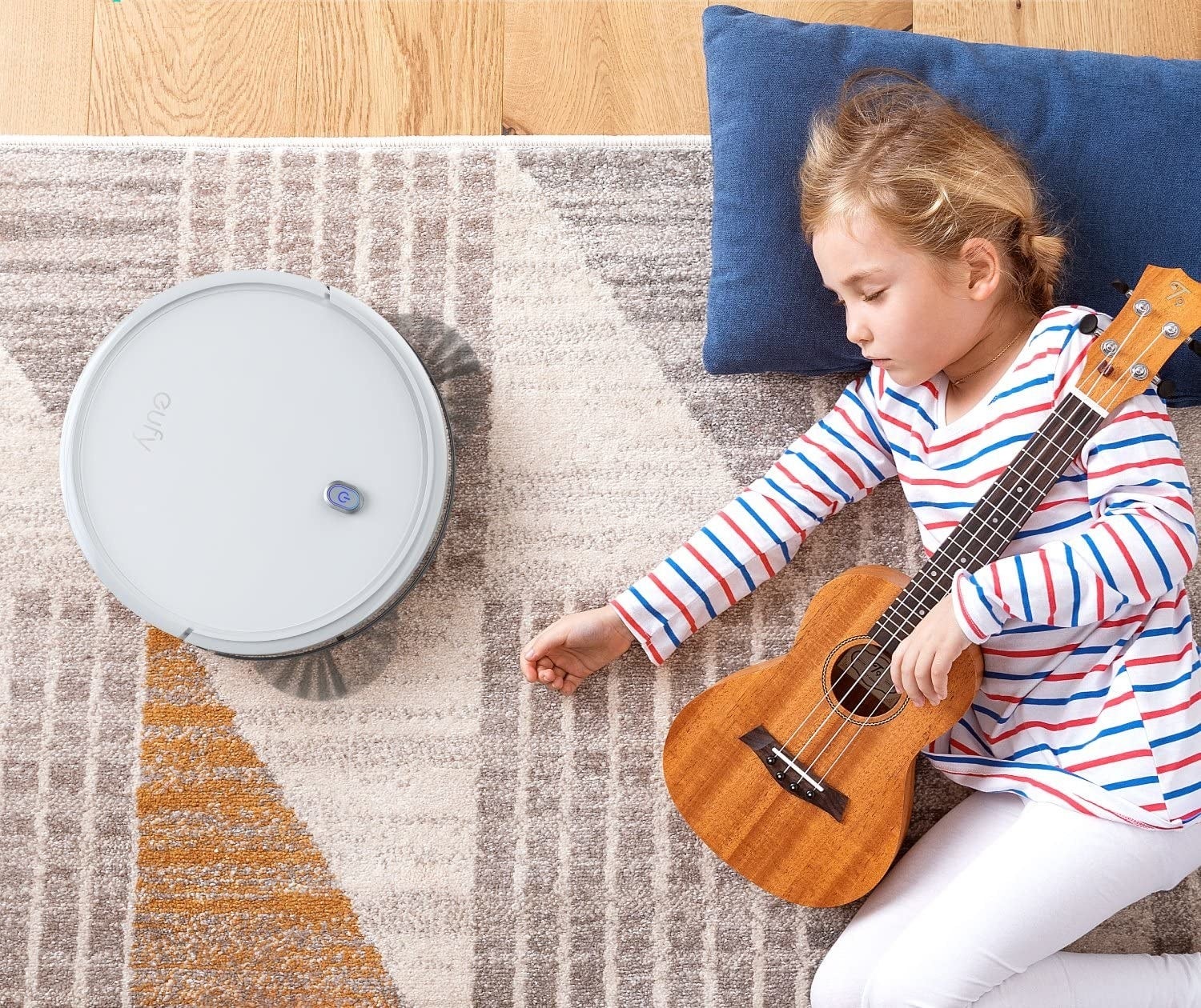 A child lying on the floor with a robot vacuum cleaning the rug beside them