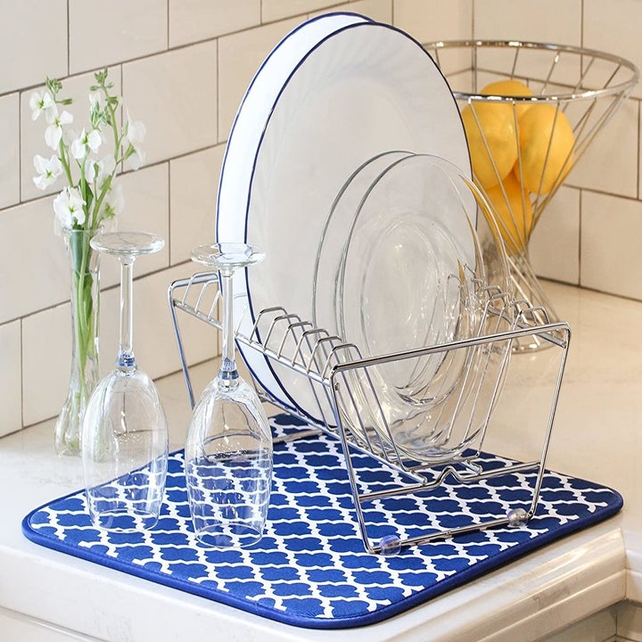 A dish drying rack full of dishes and two wine glasses on top of a drying mat with a blue and white trellis print 