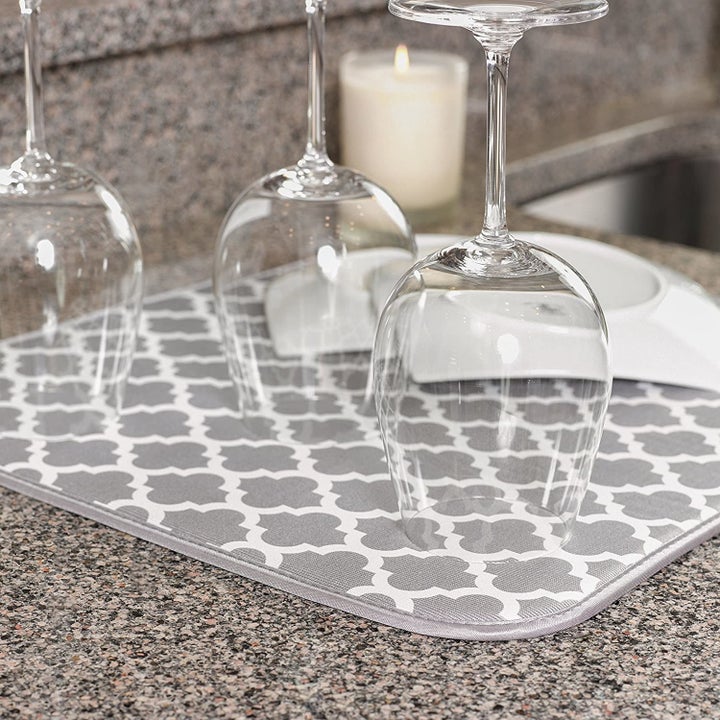 Wine glasses and a plate on top of a drying mat with a white and gray trellis print.