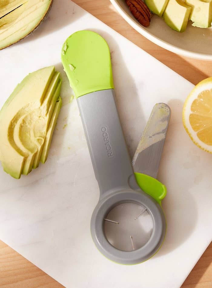 A avocado slicing tool with a spatula at one end a pit tool on the other end and a retractable knife on the side