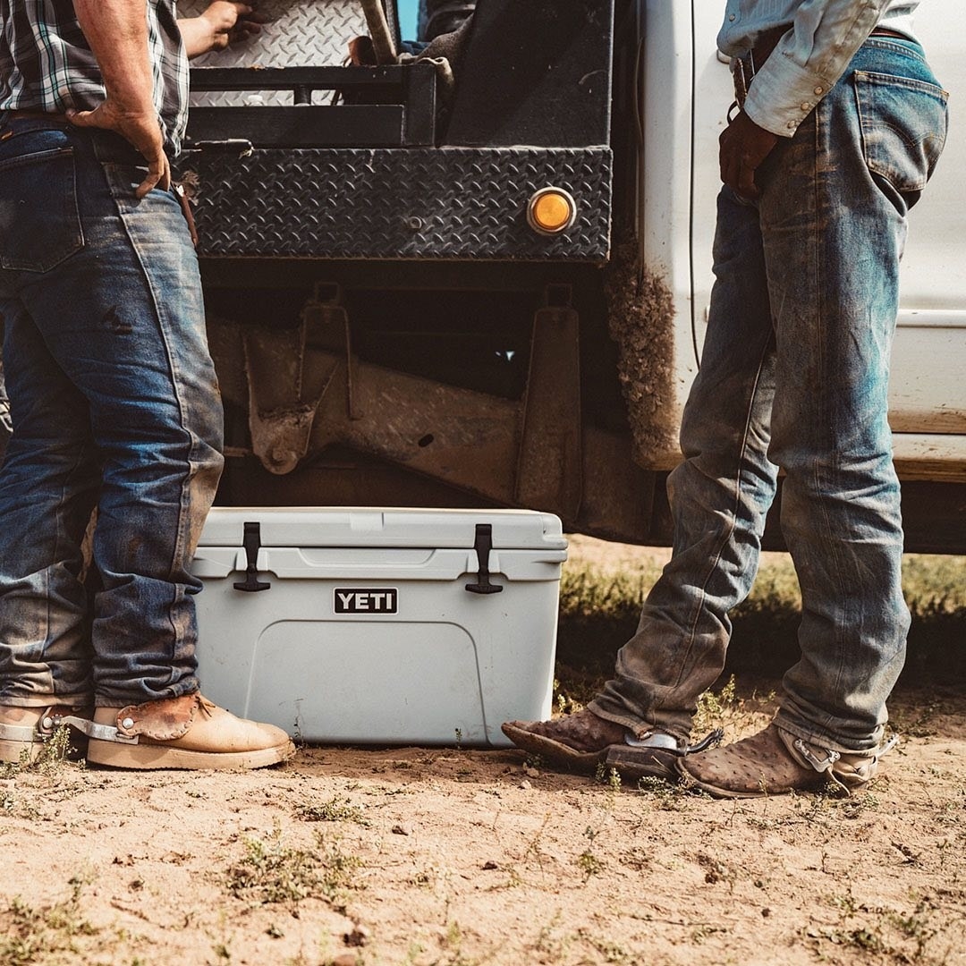 the big cooler in a sage green on the ground next to two rugged men's legs