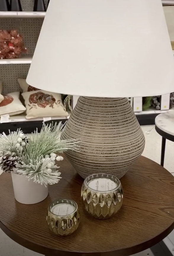 Side circle table with a large lamp, pine cones, and candles