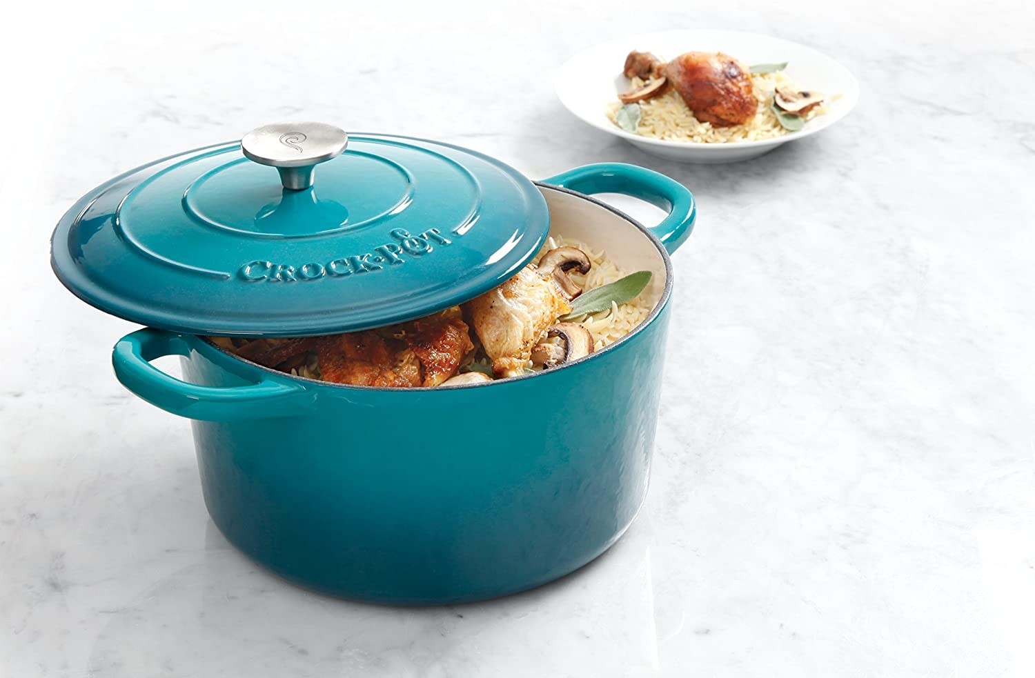 The teal dutch oven with handles and a chicken and rice dish inside