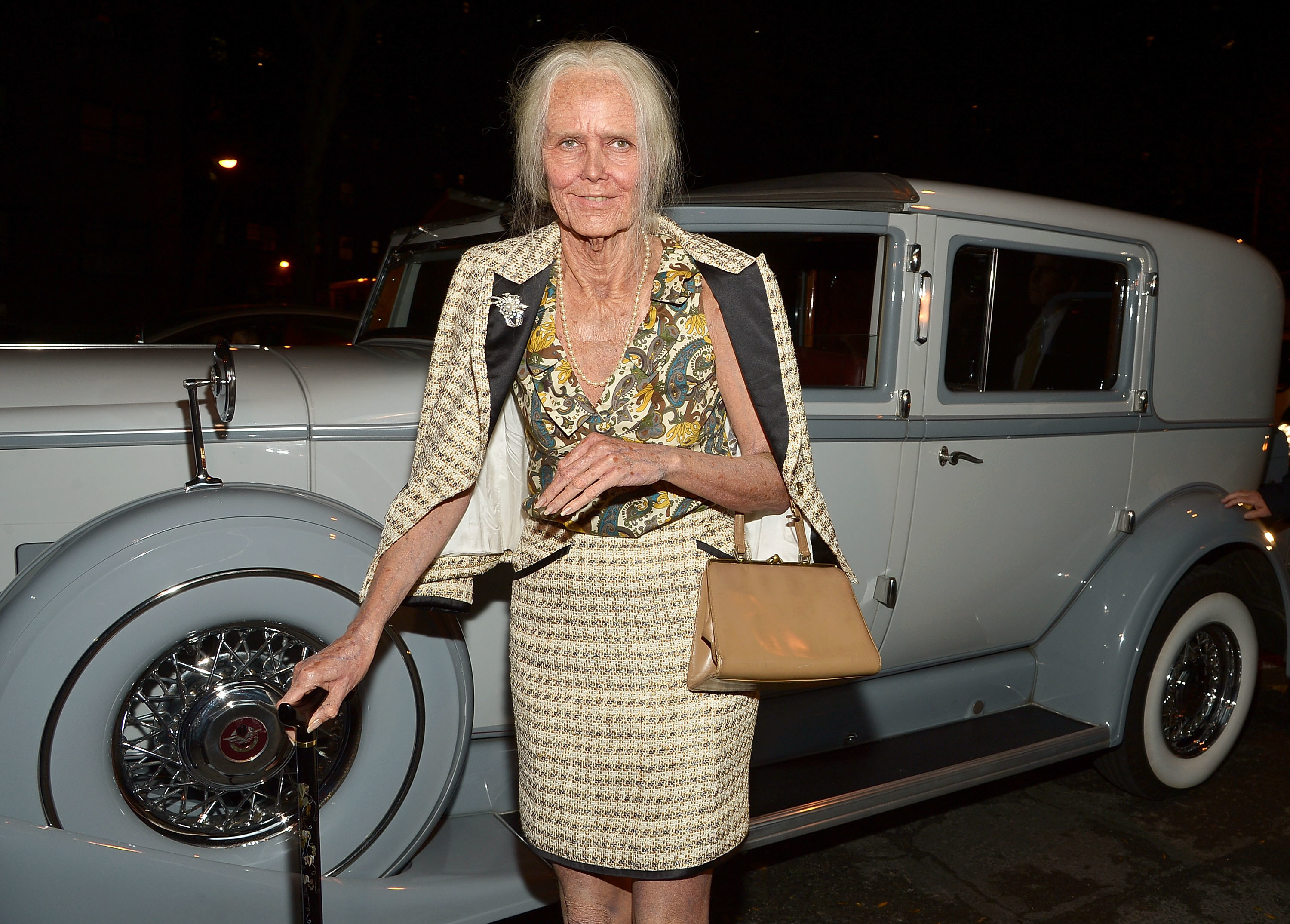 Heidi Klum dressed as an old woman in front of a fancy blue car. 