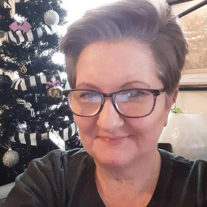 Image of Vicki Landers wearing black rimmed glasses and a small hoop earring on her right ear. She has short dark gray hair that sweeps over the top. Behind her is a decorated Christmas tree and a framed picture on the wall.