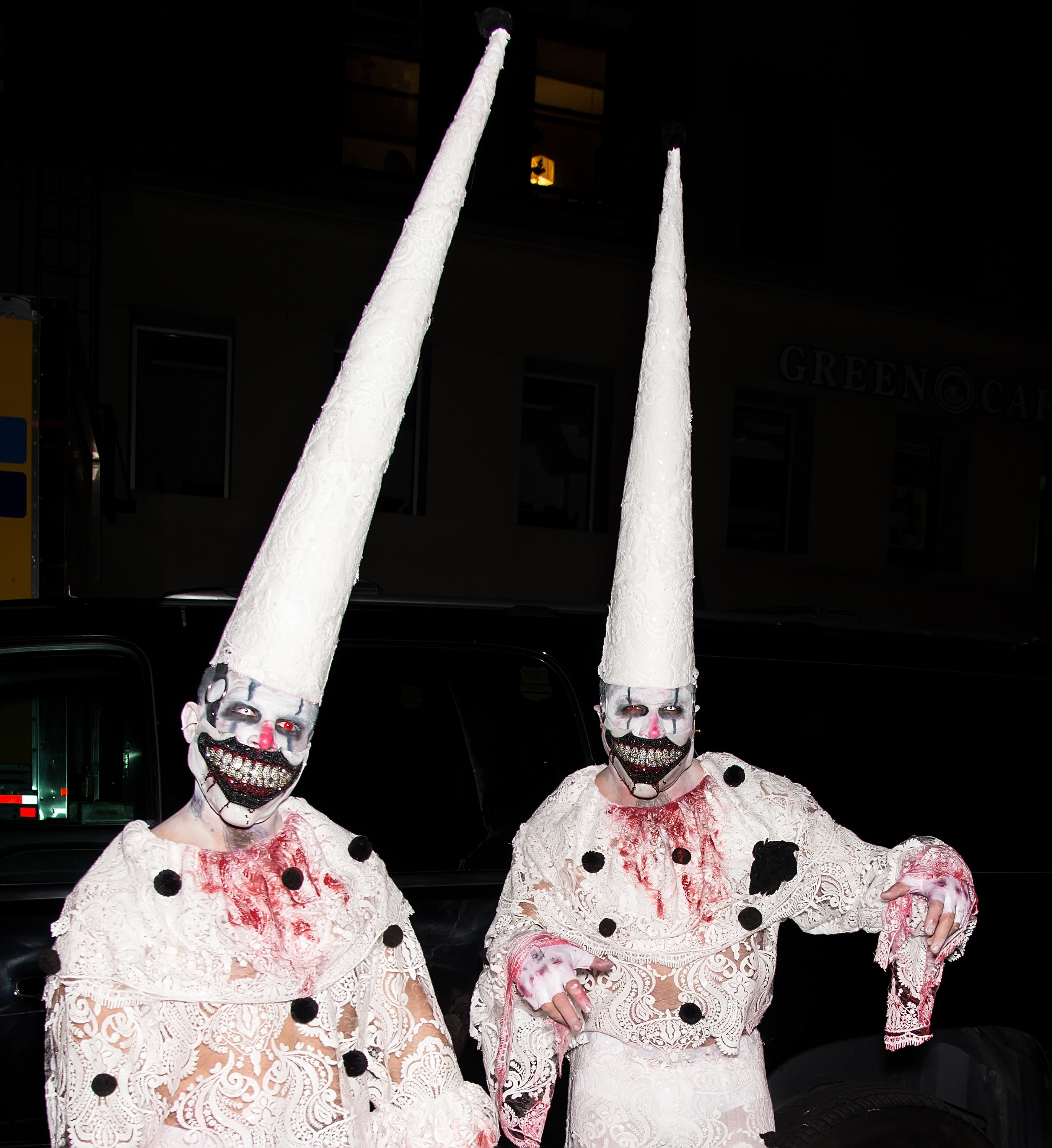 Two men dressed as very creepy clowns with lace suits and pointy hats.