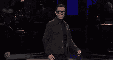 Fred Armisen exaggeratedly walks across the main stage on SNL