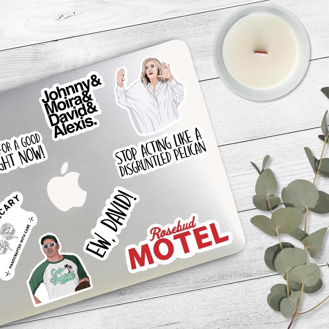 The vinyl stickers on the top of a laptop next to a candle and eucalyptus 