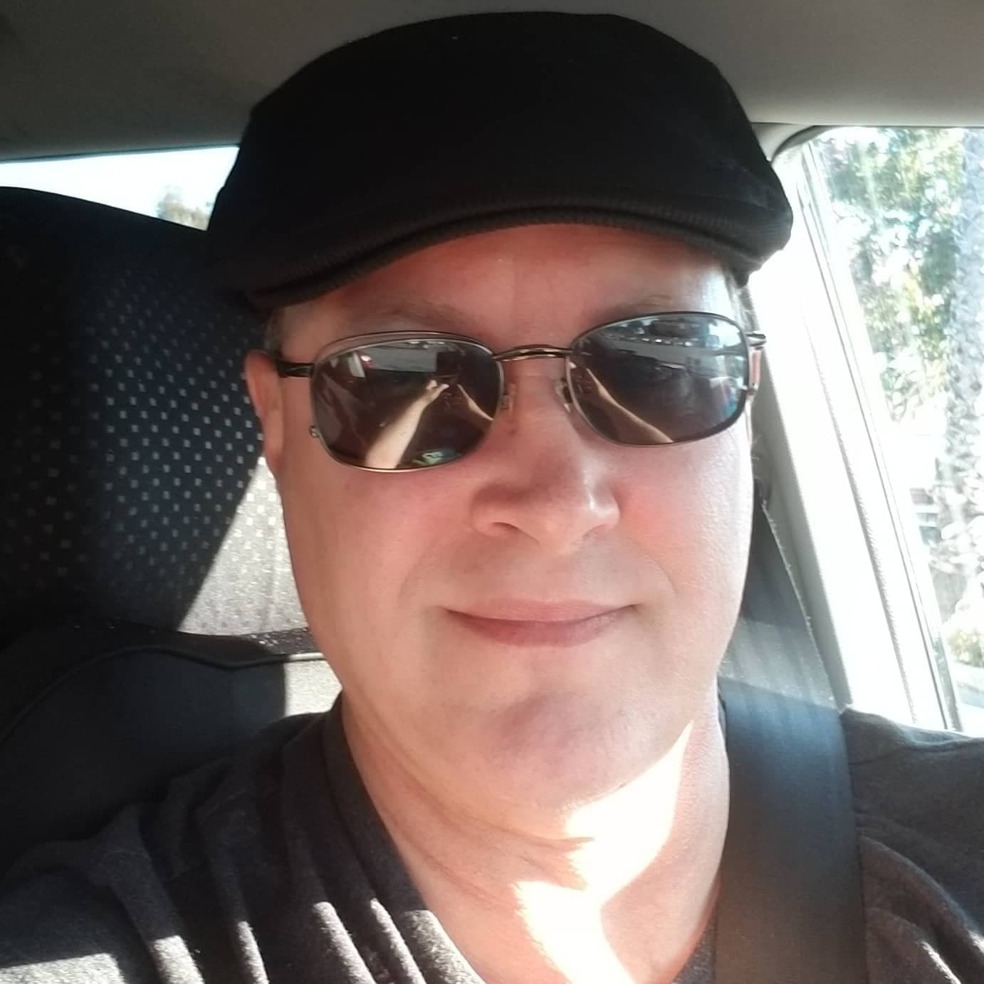 An Uber driver named Jeffrey Grant wears a black cap and sunglasses inside his car