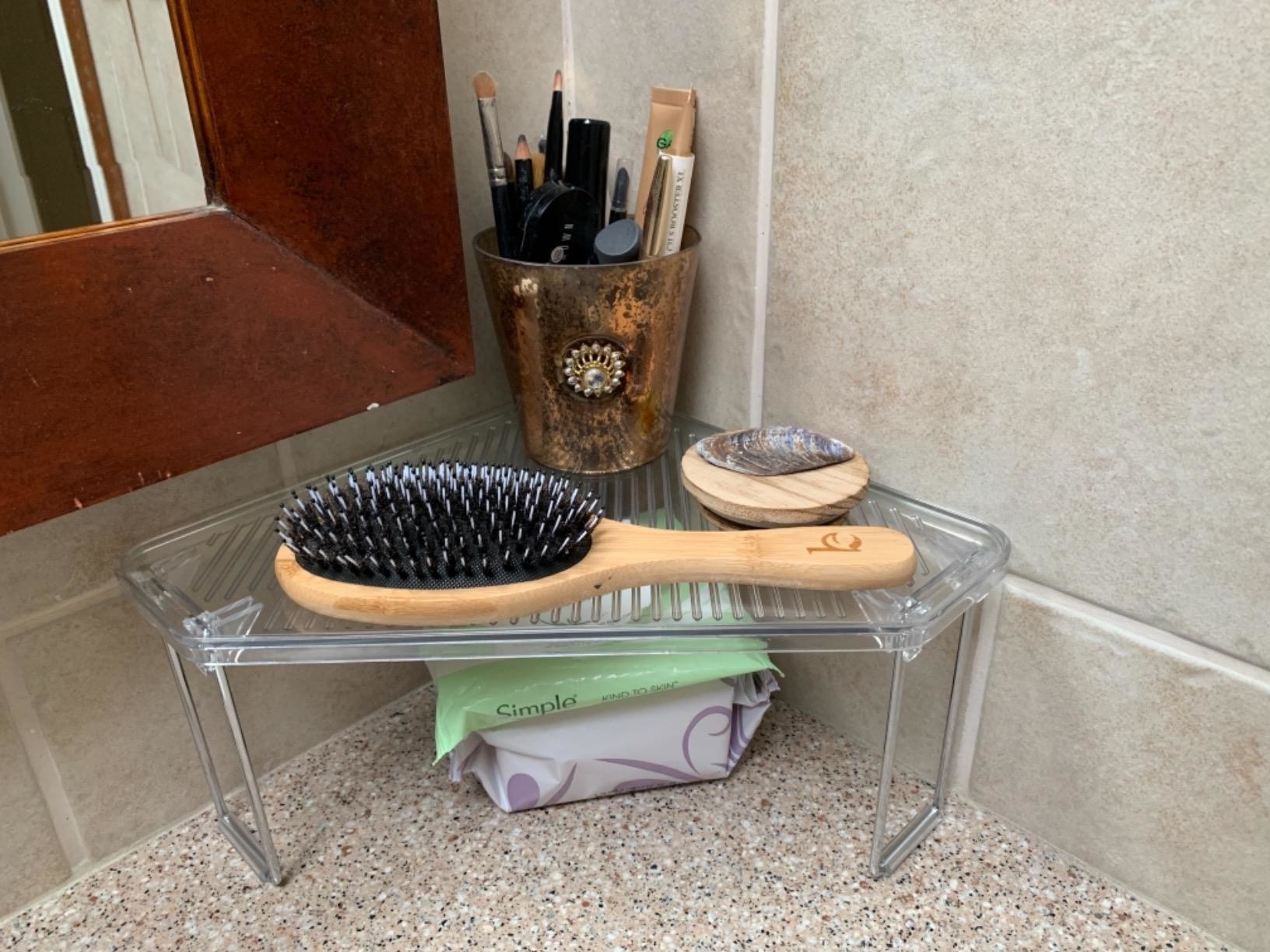 Reviewer photo of the clear shelf holding a hair brush and some makeup brushes
