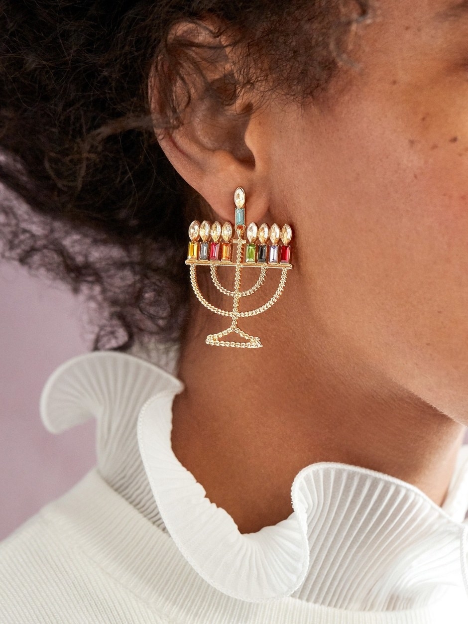 A model wearing the gold menorah with colorful jeweled candles earrings