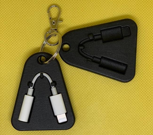 Two of the black, flat, rounded triangular cases with a dongle-shaped slot, one of which is holding a dongle, clipped to a keyring