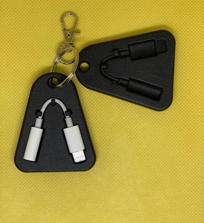 Two of the black, flat, rounded triangular cases with a dongle-shaped slot, one of which is holding a dongle, clipped to a keyring