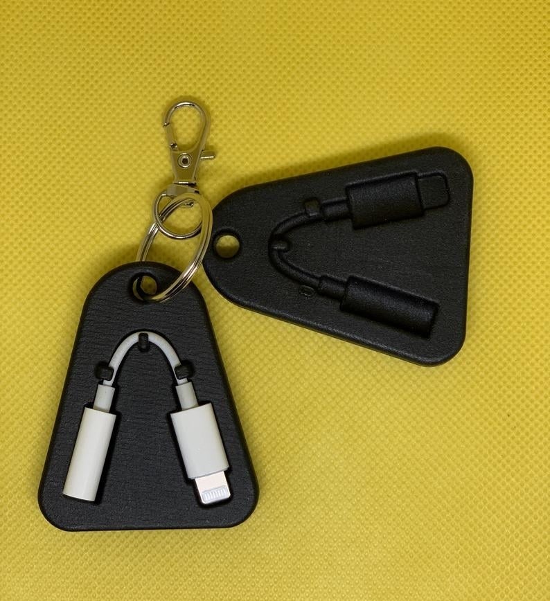 Two of the black, flat, rounded triangular cases with a dongle-shaped slot, one of which is holding a dongle, clipped to a keyring