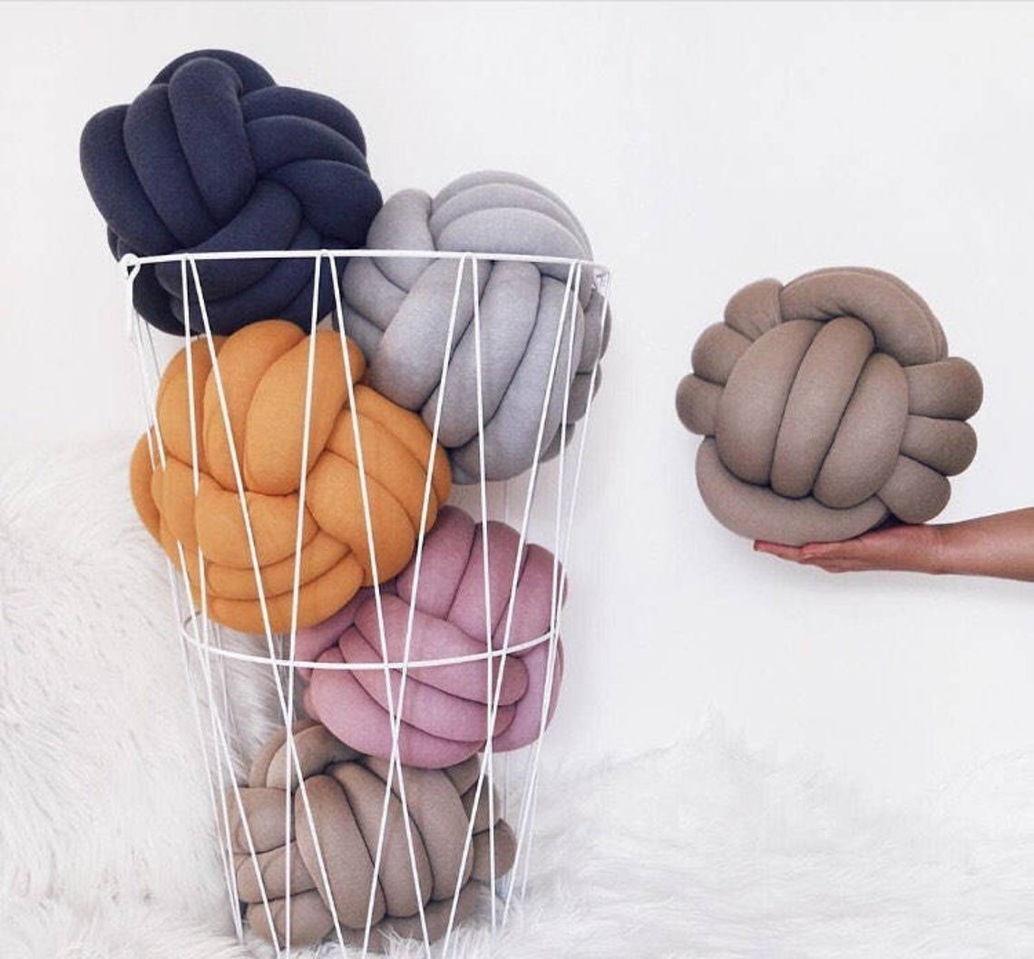 Several knotted pillows in a basket and a person holding one
