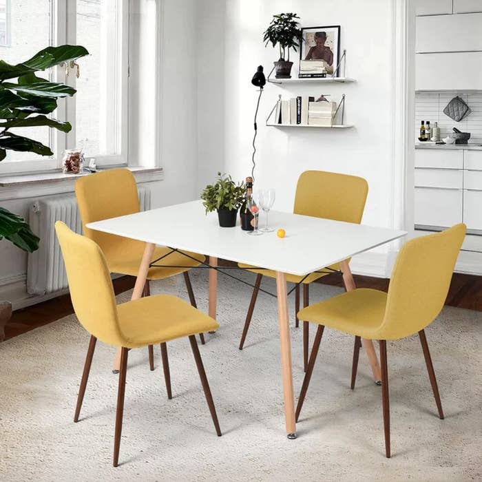 The upholstered chairs in yellow positioned around a white dining table