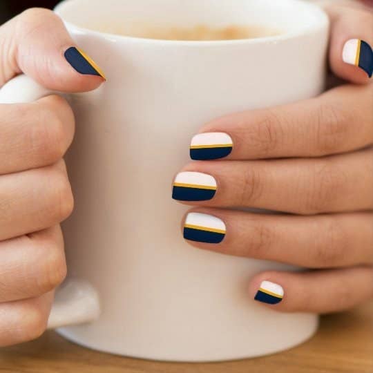 a model holding a mug with nails that feature stripes of blue gold and white