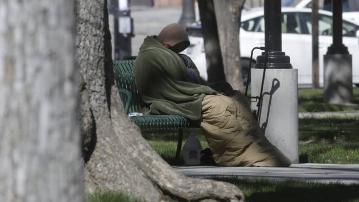 A person experiencing homelessness is wrapped in a blanket on a bench