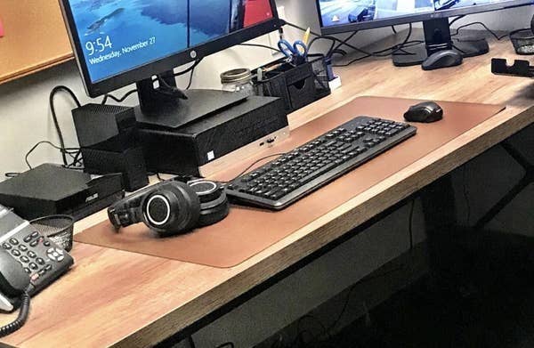 A reviewer photo of the desk pad on their desk with their keyboard, headphones, and mouse on top of it