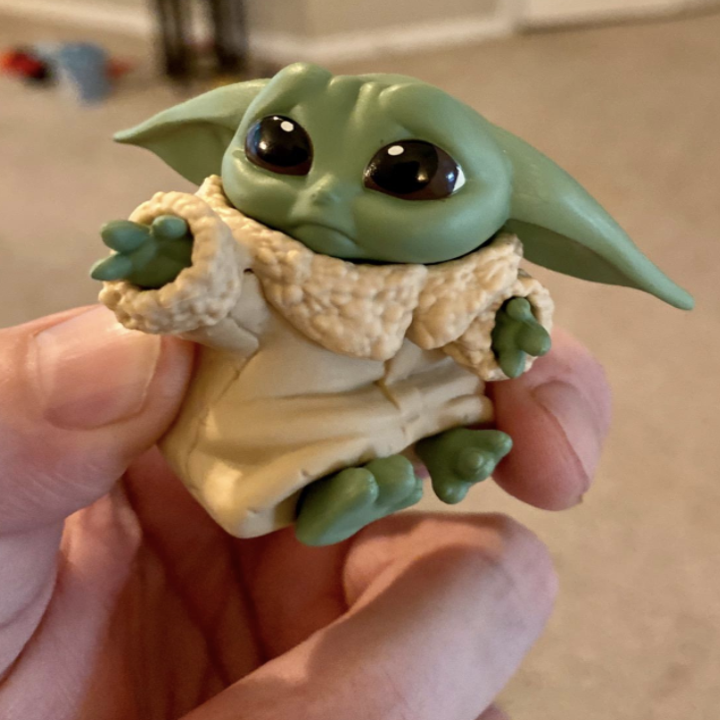 a reviewer holding a toy of baby yoda giving sad eyes