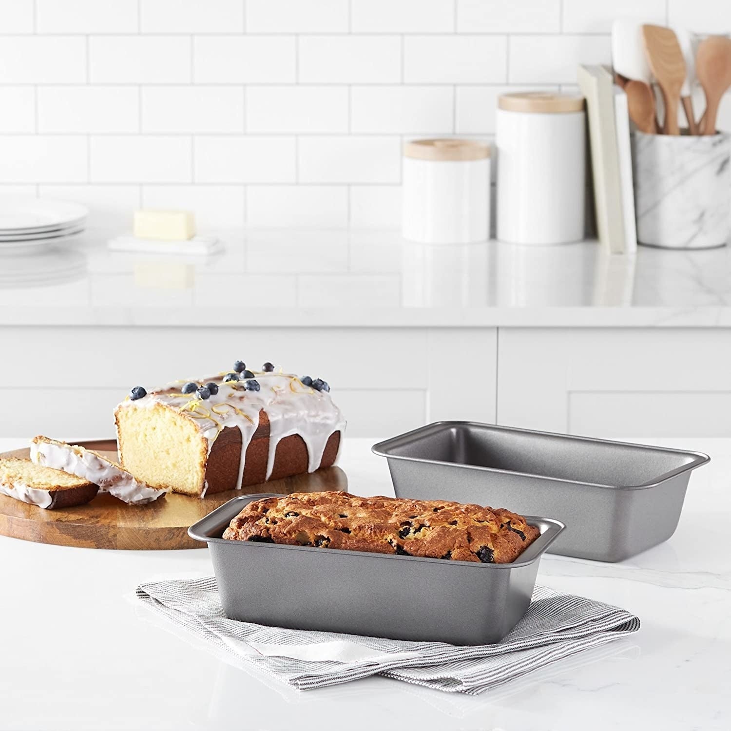 The loaf tins pictured on a kitchen counter. One empty, the other with a loaf of bread in it.
