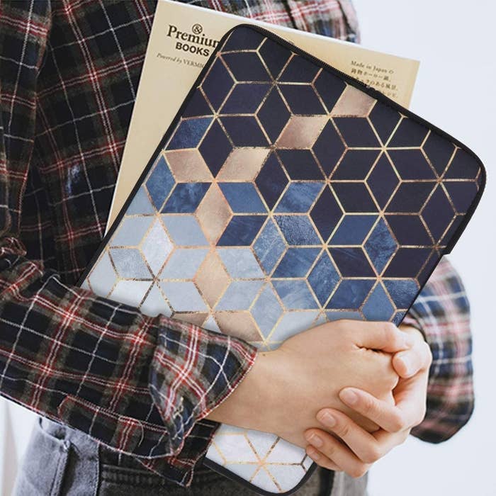 A person holds a laptop inside a geometric printed sleeve with gold accents
