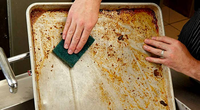 Person scrubbing sheet pan clean with pad 