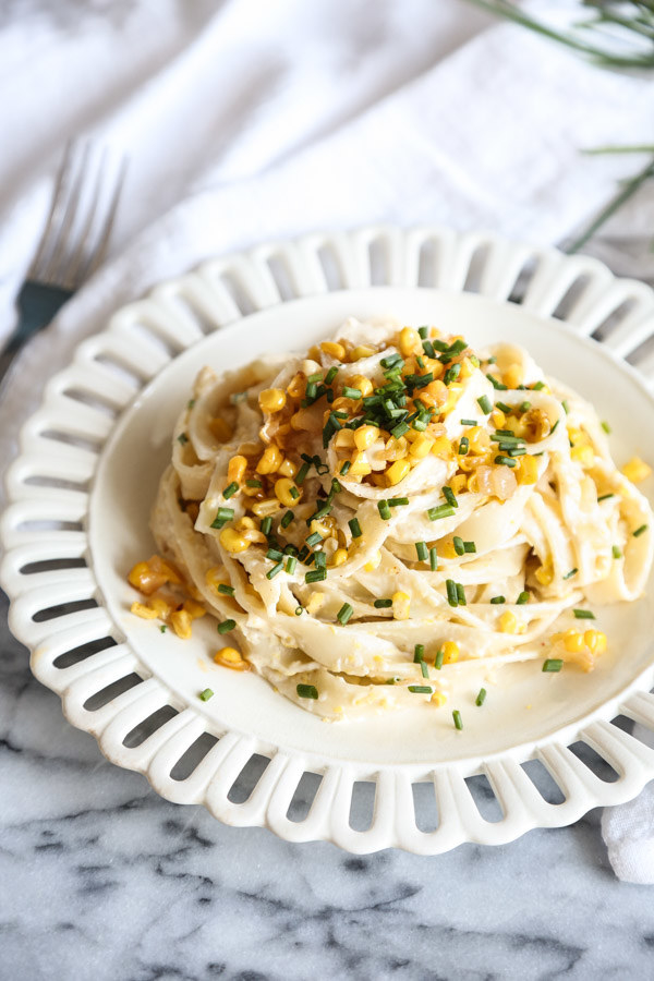 A plate of fettuccine in a ricotta sauce, topped with sweet corn and chives.
